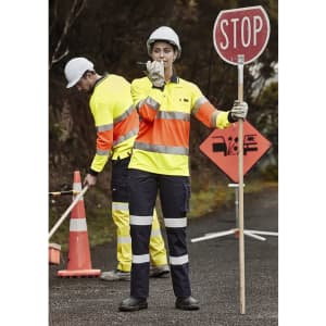 Two workers in high-visibility workwear, one holding a stop sign and the other using tools, with road signage in the background.