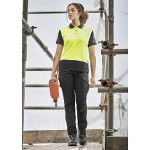 A woman wearing bright yellow and black cargo pants, standing on scaffolding with a power tool, showcasing the cargo pant design.