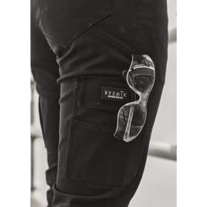 A close-up of black cargo pants with a logo and clear sunglasses tucked into the pocket.