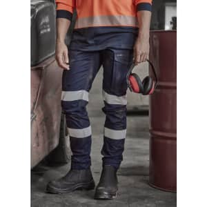A pair of navy women's cargo pants with reflective stripes, cuffed at the ankles, held by a person wearing work boots.