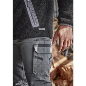 A close-up of men's grey work pants featuring multiple pockets and a zipped side pocket, paired with a black fleece top.