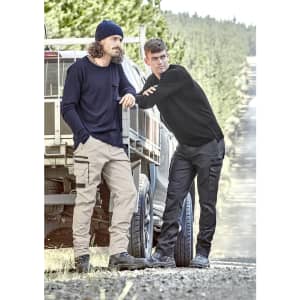 Two men wearing work pants in beige and black, standing beside a vehicle in a forested area. Both have casual attire and a logo on the clothing.