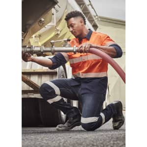 A worker in orange and navy striped attire kneels beside a tanker, wearing Mens Bio Motion Taped Stretch Jeans.