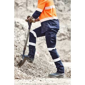 Mens essential stretch cargo pant in navy, featuring reflective stripes, worn with work boots and an orange high-visibility shirt.