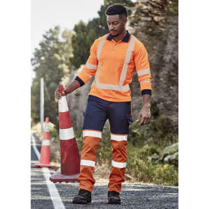Hi-vis orange and navy work pants with reflective tape, worn by a man holding a traffic cone on a rural road.