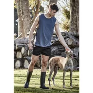A man in a grey tank top and black shorts interacts with a greyhound in a natural outdoor setting.