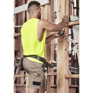 A man wearing khaki cargo shorts and a bright yellow sleeveless top, working with tools on a construction site.