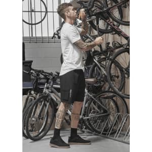 A man stands in a garage adjusting a bike, wearing black Men's Streetworx board shorts and a white t-shirt.