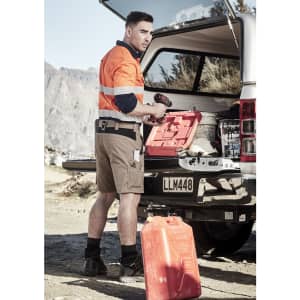 A man in an orange high-visibility shirt and beige shorts stands by an open vehicle boot, holding a tool.
