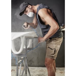 A man wearing a mask and cap works with an air tool, dressed in rugged khaki stretch shorts with a logo.