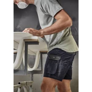 A man wearing navy rugged cooling stretch shorts and a grey t-shirt, working at a table with a surfboard.