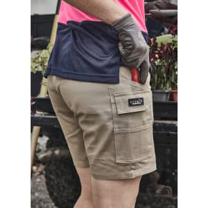 A person wearing khaki women's cargo shorts with a logo, holding gardening tools and dressed in a pink and navy top.