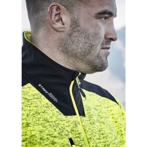 A close-up of a man wearing a bright yellow and black reinforced knit 1/2 zip pullover, featuring a branding logo.