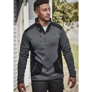 A man wears a grey and black Unisex Streetworx Reinforced Knit 1/2 Zip Pullover, featuring a zippered pocket and side pockets.
