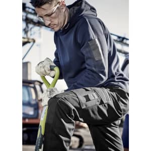 A man in a navy blue unisex multi-pocket hoodie, wearing gloves, kneels with a spade in a work environment.