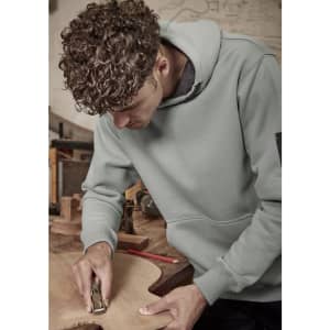 A unisex multi-pocket hoodie in green worn by a person working on wood, featuring a logo on the sleeve.