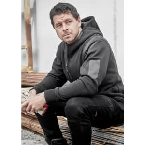 A black unisex zip front hoodie with multi-pockets, featuring a logo, worn by a seated man.