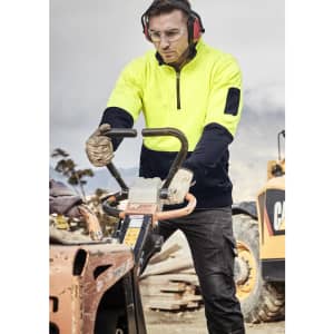 A man wears a high visibility yellow and navy unisex 1/2 zip pullover while operating machinery on a work site.