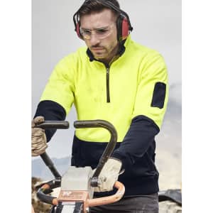 A unisex hi-vis yellow and navy 1/2 zip pullover, featuring a logo and worn by a person operating machinery.