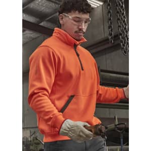 An orange unisex 1/4 zip pullover is worn by a person inside a workshop, featuring protective glasses and gloves.