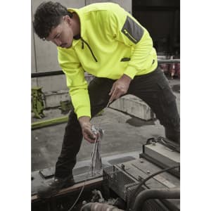 A man wearing a bright yellow water-resistant 1/4 zip pullover is working on machinery. The pullover has a logo.