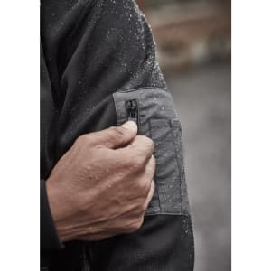 A close-up of a hand adjusting the zipper on a black water-resistant hoodie, showing droplets of water on the fabric.