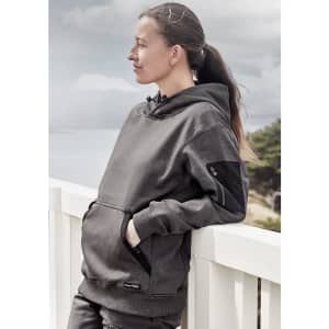 A unisex water-resistant hoodie in dark grey, featuring a front pocket and logo, worn by a woman outdoors.