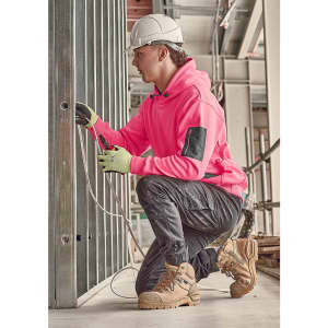 A person in a bright pink water-resistant hoodie and grey work pants kneeling, working on electrical wires in a construction setting.