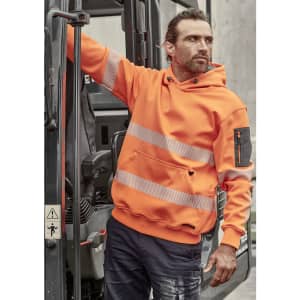 An orange water-resistant hoodie features segmented tape and a logo, worn by a model near machinery.