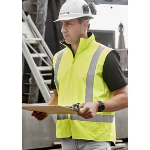 A man wearing a bright yellow waterproof reversible vest with reflective stripes, holding a clipboard.