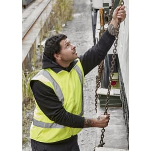 A man in a high-visibility yellow waterproof reversible vest is operating a chain while standing on a gravel surface.
