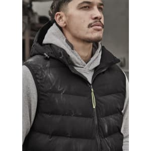 A unisex black hooded puffer vest is worn over a grey hoodie. The vest features a logo and a zip closure.