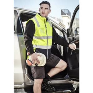 A unisex hi-vis softshell vest in fluorescent yellow with reflective stripes, worn by a man exiting a vehicle.