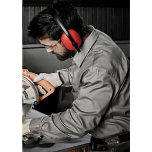 A man wearing a grey long sleeve shirt and safety gear operates a power saw in a work environment.