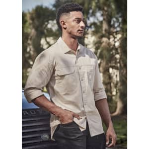 A lightweight long sleeve shirt in beige, featuring a front pocket and a logo. Set outdoors with greenery in the background.
