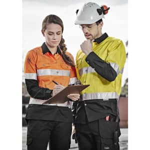 Two workers in high-visibility long sleeve shirts, one orange and one yellow, discussing a clipboard while wearing protective gear.