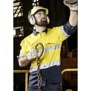 A man wearing a high-visibility yellow and navy long sleeve shirt with reflective tape, safety glasses, and hearing protection.