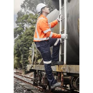 A man wearing an orange flame lightweight ripstop taped shirt climbs a ladder on a train, surrounded by greenery.