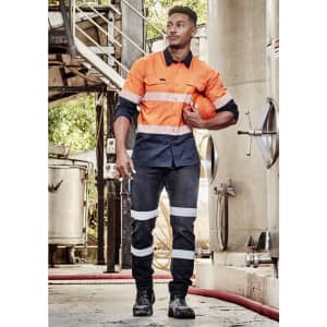 A worker in an orange and navy long sleeve shirt with segmented tape, holding a helmet in an industrial setting.