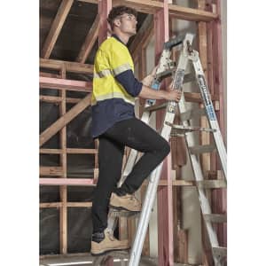 A man in a blue and yellow long sleeve shirt climbs a ladder in an under-construction area. The shirt features reflective segments.
