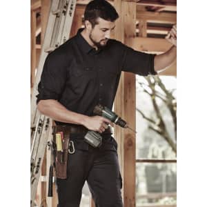 A man in a black rugged long sleeve shirt is holding a power drill, standing inside a construction site.