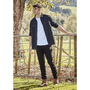 A long sleeve black button-up shirt worn over a white t-shirt, paired with black pants and boots, outdoors.