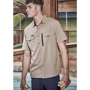 A tan short sleeve button-up shirt with two front pockets and a zip pocket, worn by a male model.