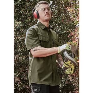 A man wearing an olive green short sleeve button-up shirt, safety glasses, and ear protection, using a power tool.