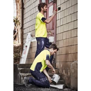 A high visibility yellow safety tee worn by two men painting a wall, one standing and one kneeling, with painting supplies.