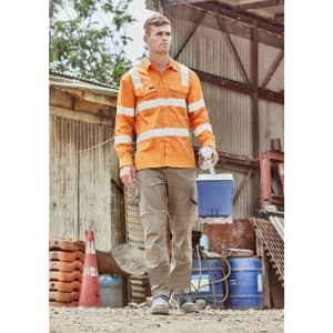 A man wears an orange long sleeve work shirt with reflective stripes, carrying a blue cooler in an outdoor setting.