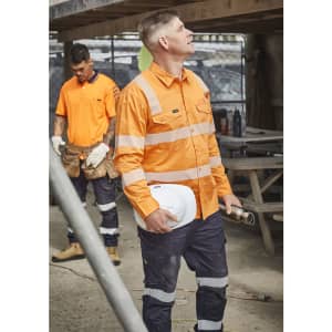 A bright orange men's work shirt with segmented tape, paired with navy pants, worn by a worker on site.