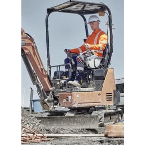 A worker in a high-visibility orange shirt and white hard hat operates a small excavator on a construction site.