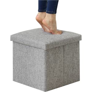 A grey foldable storage ottoman with a textured fabric, featuring a person’s bare feet on top.