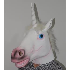 A unicorn mask in white with a pink snout, blue eyes, and a horn, worn by a person against a plain background.
